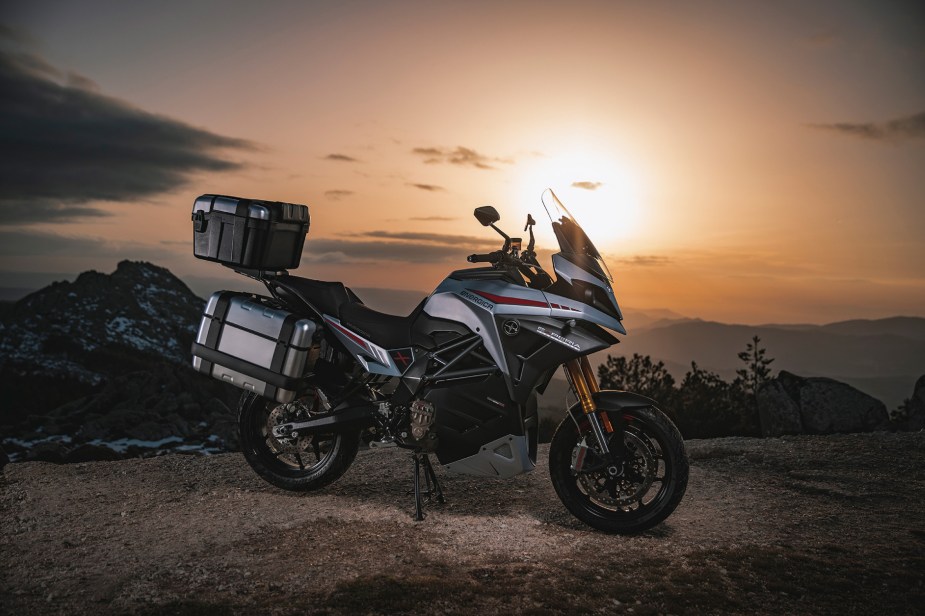 The side view of a gray-and-red 2022 Energica Experia with luggage on its center stand in the desert