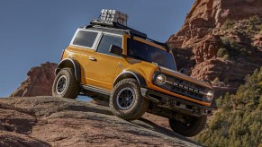 A yellow 2022 Ford Bronco small off-road SUV is driving on a rock.