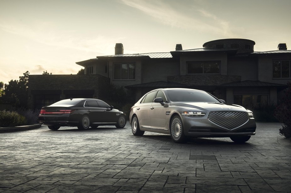 A silver and a black 2022 Genesis G90 in front of a mansion