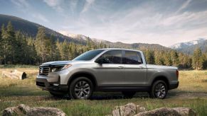 The 2022 Honda Ridgeline Sport pickup truck parked in a grassy field near hills of forest trees