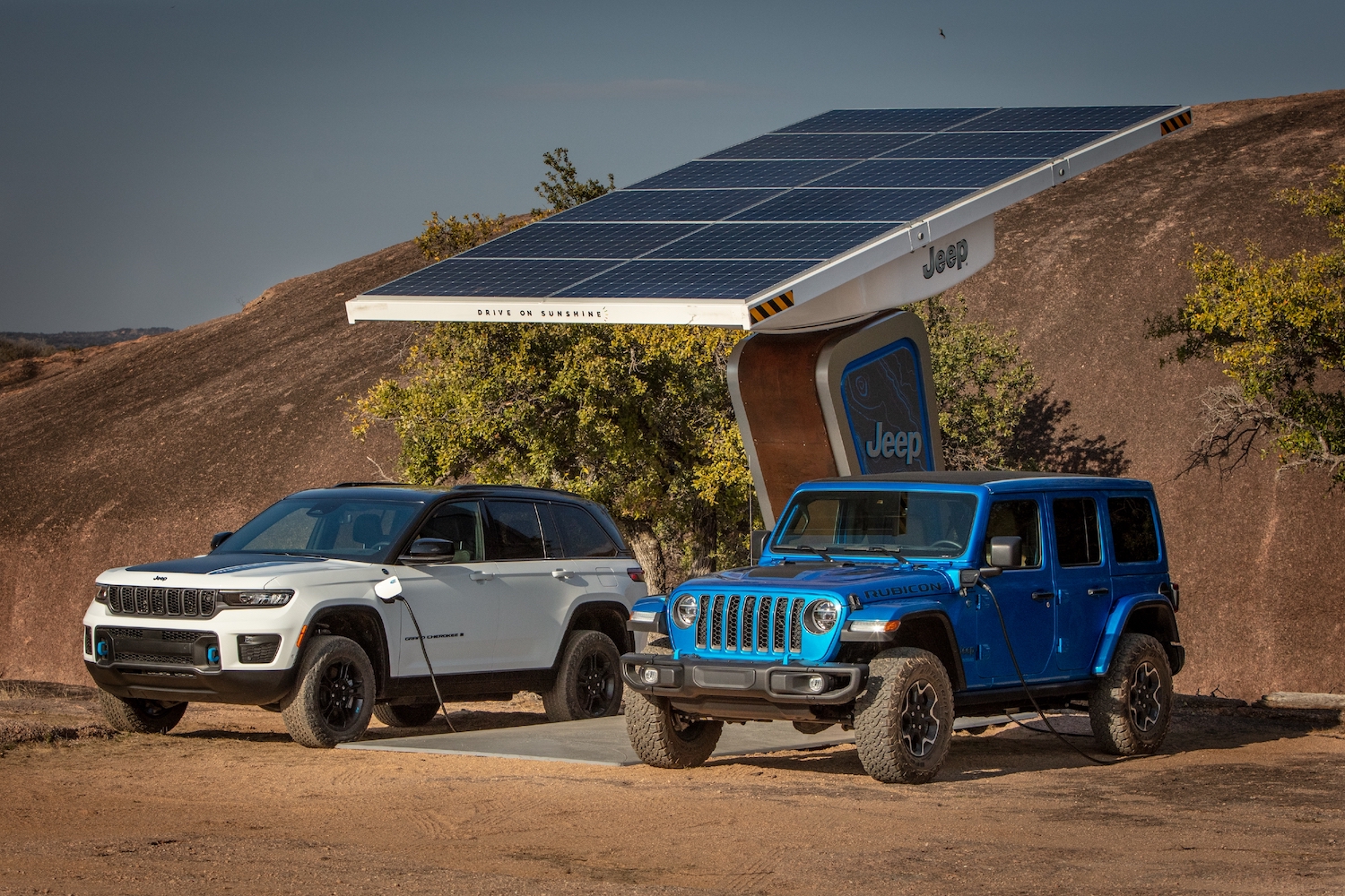 Blue Jeep wrangler and White Grand Cherokee parked side-by-side under a solar panel in the desert.