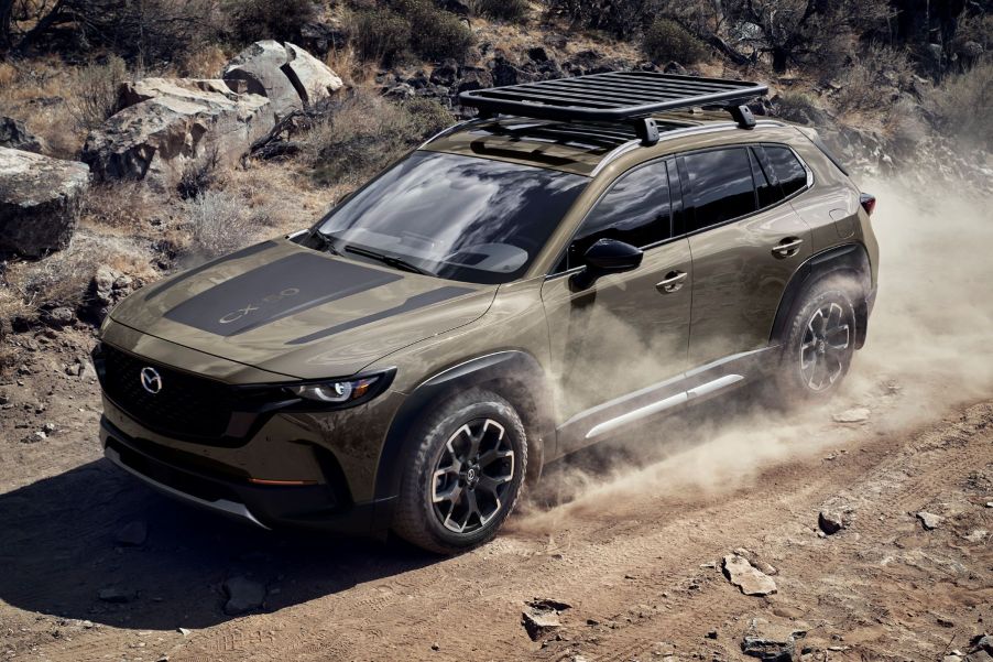 A 2023 Mazda CX-50 compact crossover SUV driving on a dirt road as dust trails around it