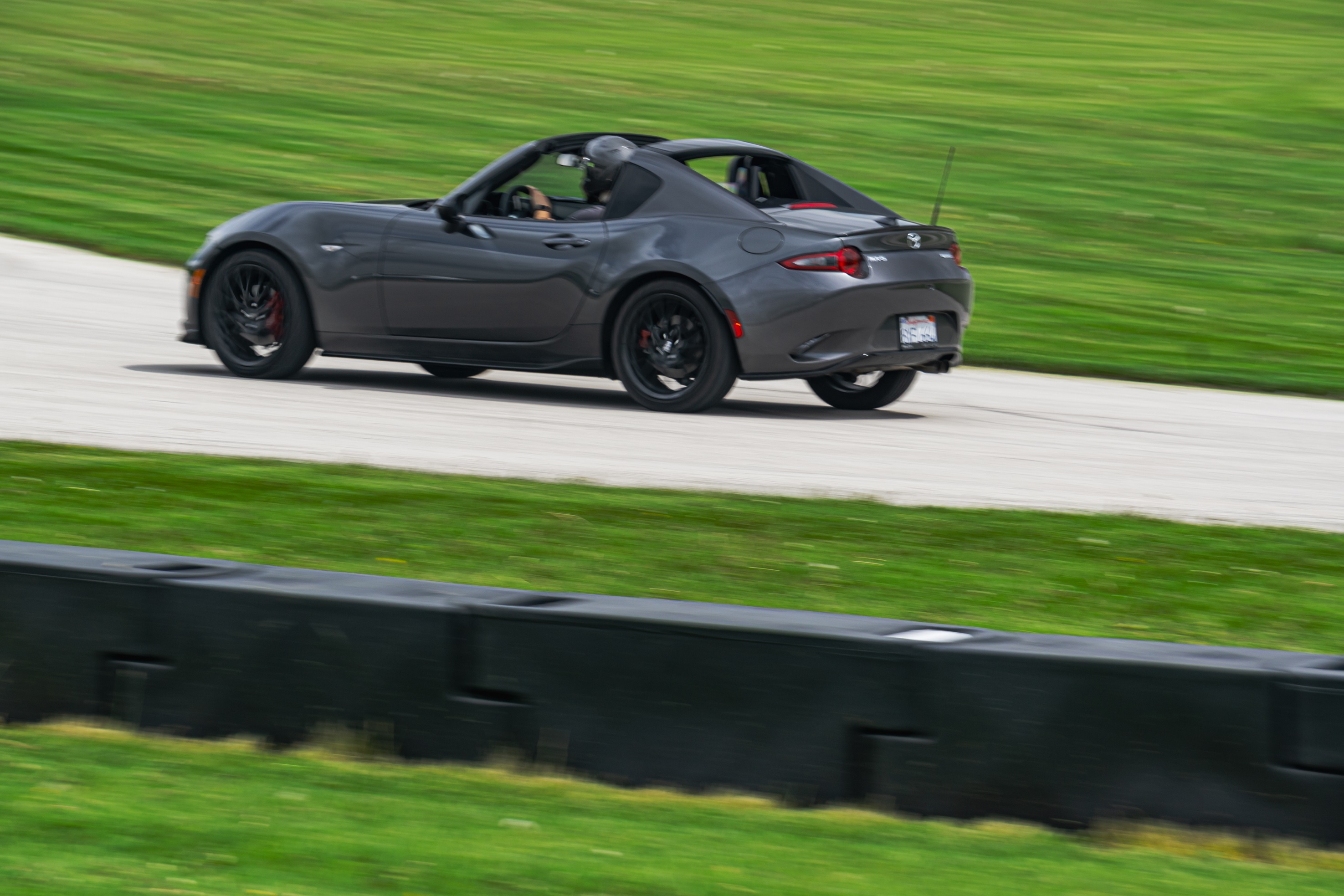 The rear 3/4 view of a gray 2022 Mazda MX-5 Miata RF Club going around a racetrack corner