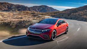 A red 2022 Mercedes-Benz AMG EQS all-electric (EV) sedan driving down a highway near hills