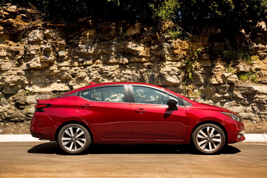 A side shot of a red 2022 Nissan Versa subcompact sedan parked near a stone cliffside