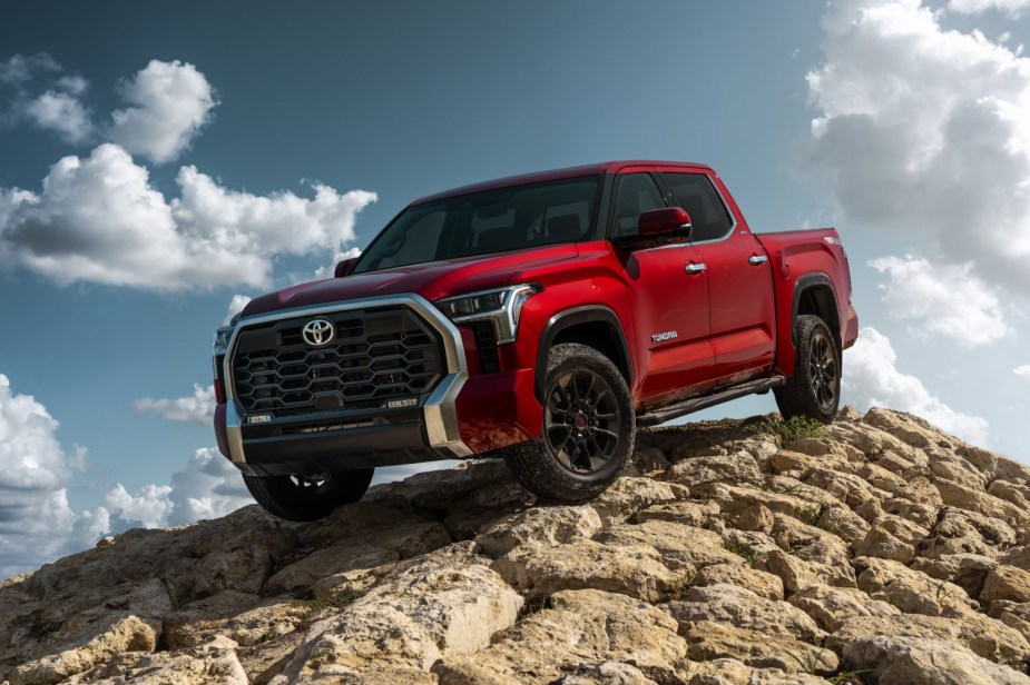 Red Toyota Tundra 4x4 pickup truck parked an top of a pile of rocks, clouds visible behind.