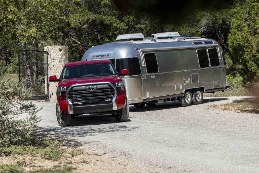 Red Toyota Tundra pickup truck towing an airstream camper trailer down a wooded road.