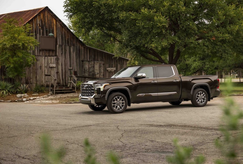 Mesquite brown 1794 Edition Toyota pickup truck parked in front of a barn for a publicity photo, trees visible in the background.