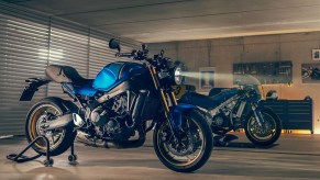 A blue-and-black 2022 Yamaha XSR900 in a garage in front of a blue 1980s Yamaha GP race bike