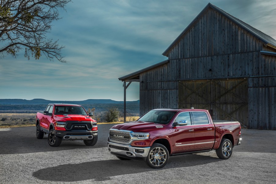 two 2022 Ram 1500 trim levels in shades of red parked near a barn