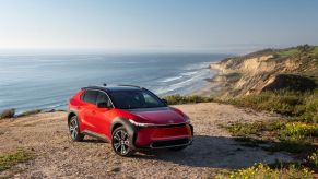 A red 2023 Toyota bZ4X Limited AWD electric SUV model parked on a sandy cliff near a seaside of crashing waves