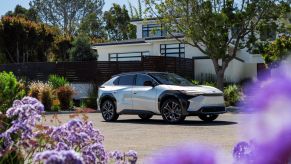 A 2023 Toyota bZ4X Limited EV/electric SUV model in Elemental Silver Metallic farmed by lavender flowers outside a house