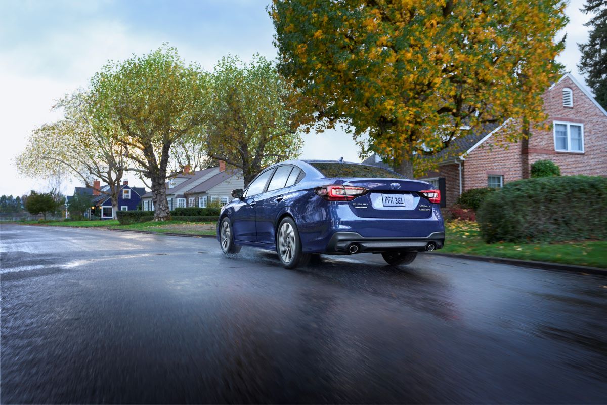 Blue 2023 Subaru Legacy midsize sedan driving away down a wet road