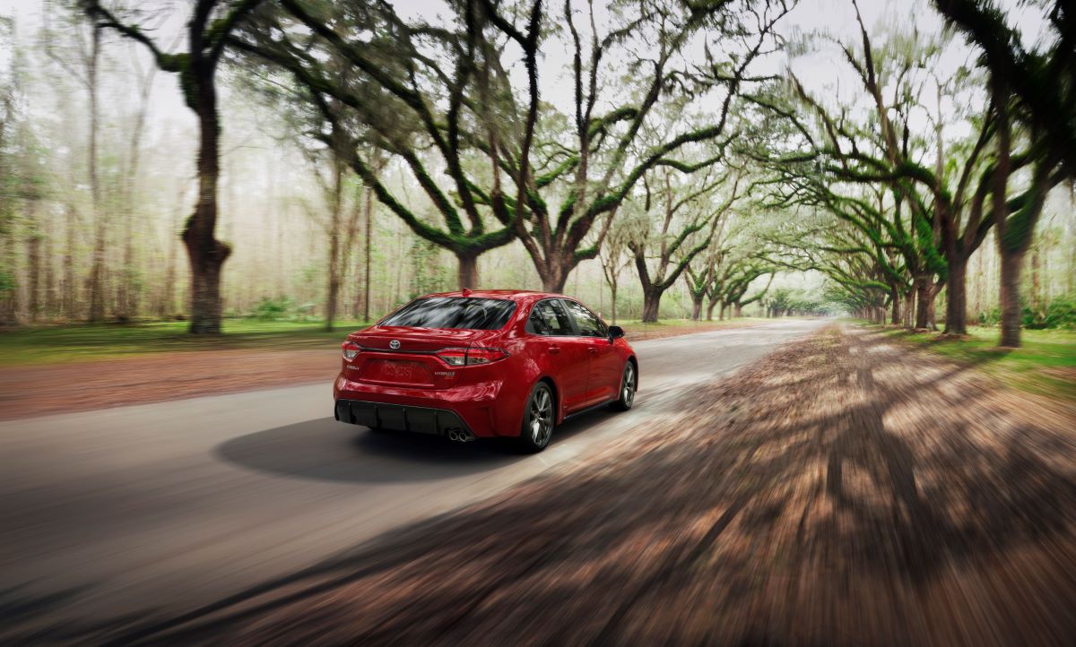 Red 2023 Toyota Corolla Hybrid AWD sedan cruising down a dirt road