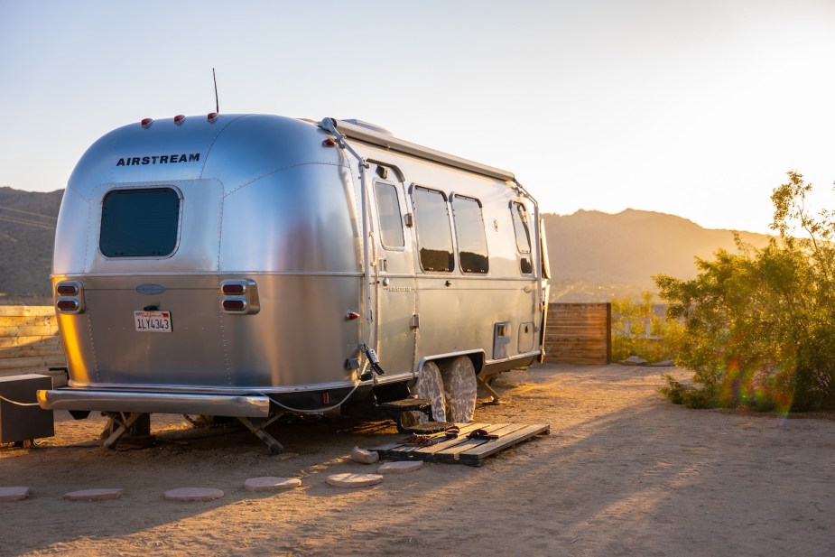 Silver Airstream camper trailer, with the sun setting over mountains in the background.