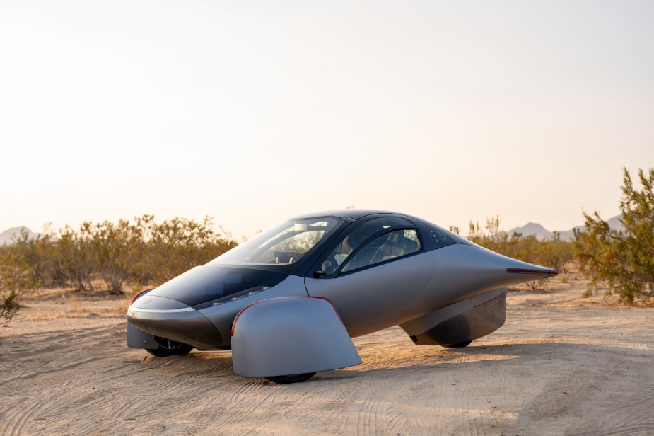 A white Aptera, with great miles of range, parked in the desert.