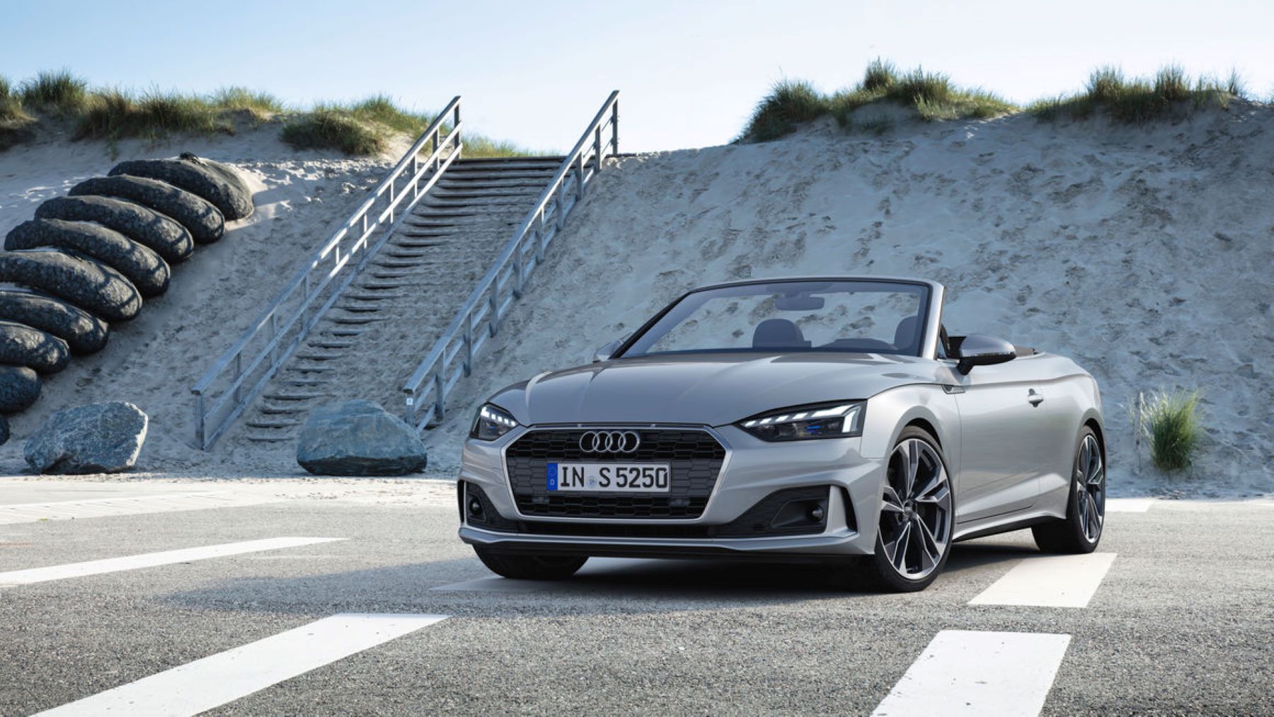 A silver-gray Audi A5 cabriolet convertible model in a parking lot next to a beach with stairs