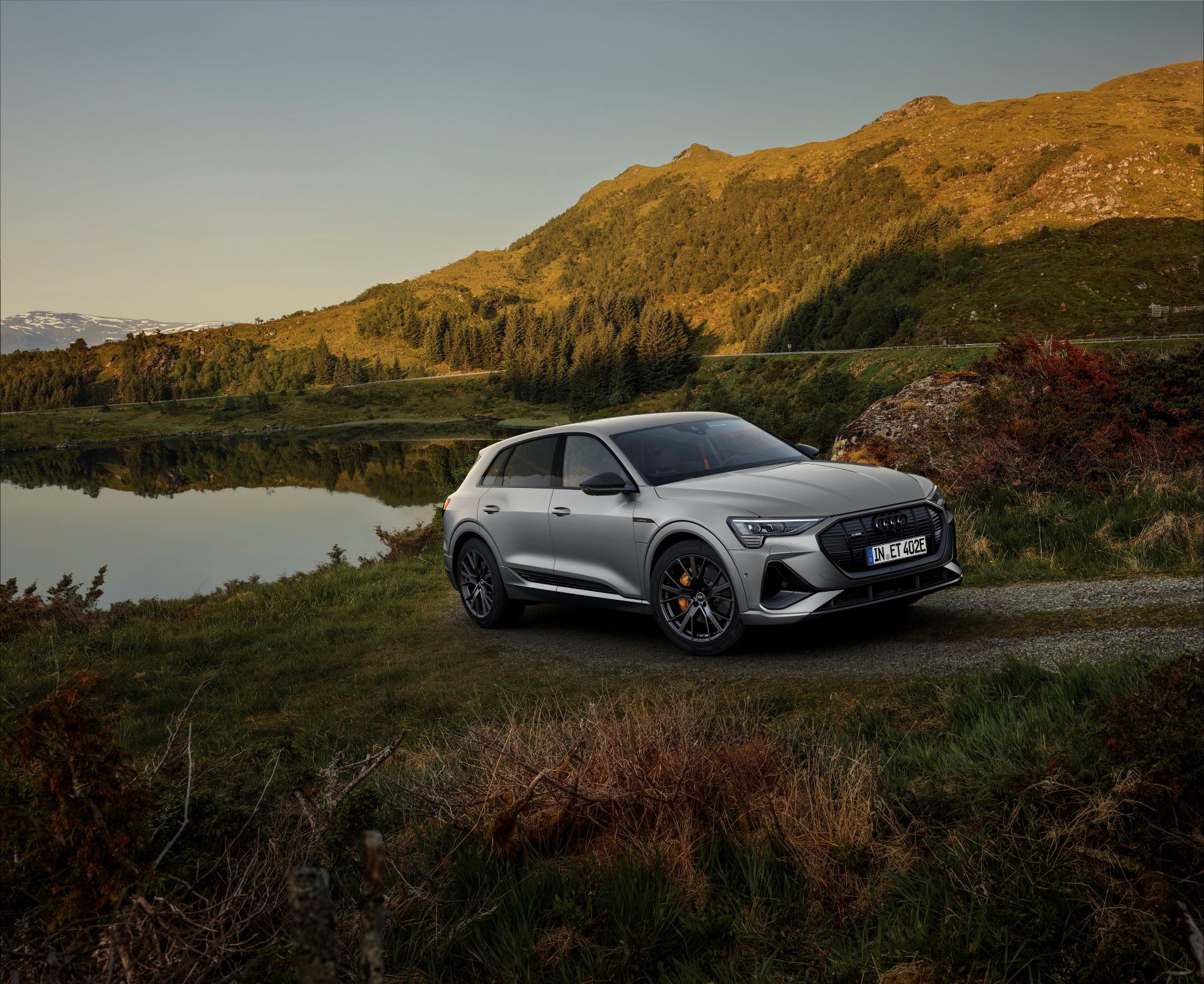 The Audi e-tron S line black edition all-electric luxury SUV driving on a gravel path near a small pond