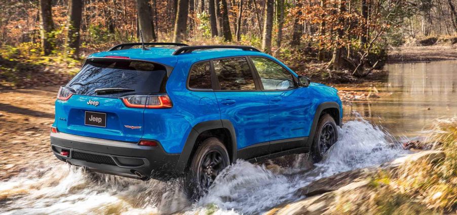 A blue 2022 Jeep Cherokee splashing through a puddle.