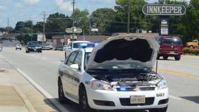 This is a white Danville Police Department cruiser car parked on a city street with its hood up and its lights on.