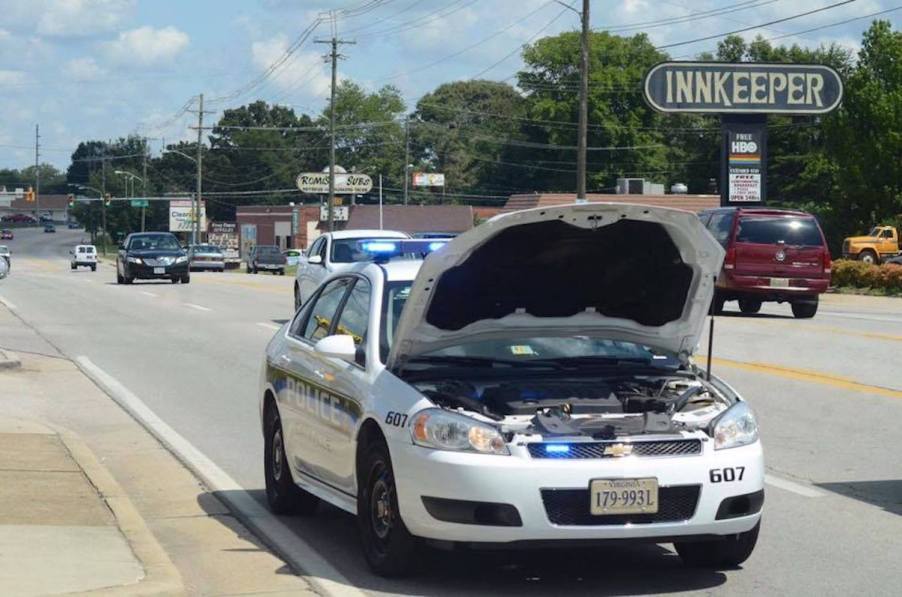 This is a white Danville Police Department cruiser car parked on a city street with its hood up and its lights on.