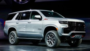 A silver Chevy Tahoe parked indoors on a black stage with a black background.