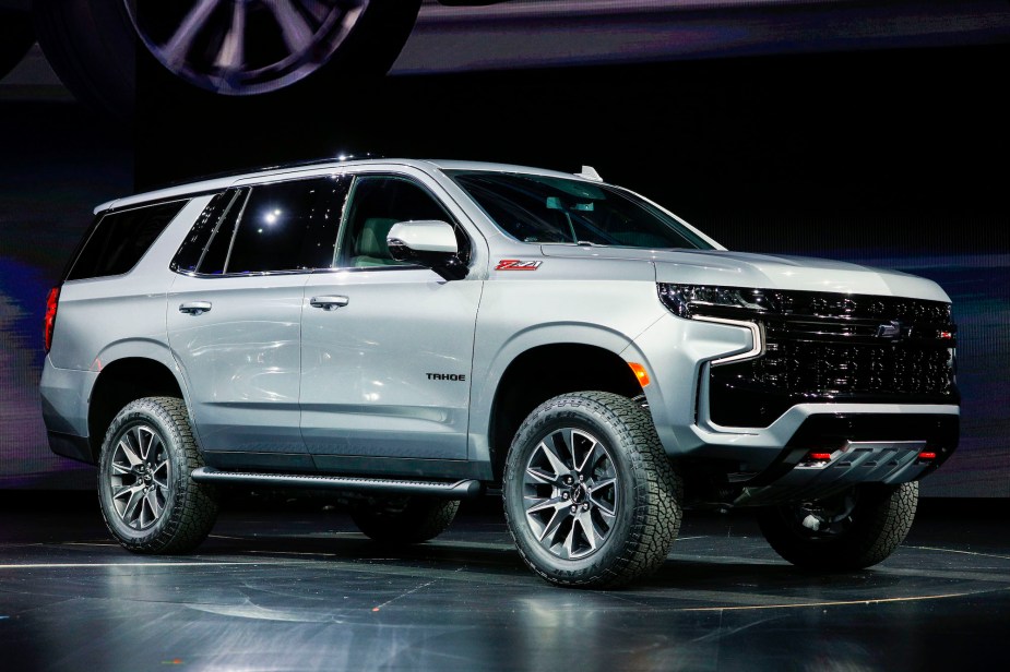 A silver Chevy Tahoe parked indoors on a black stage with a black background.