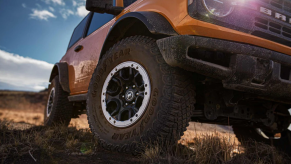 A Ford Bronco model with the Sasquatch Package parked in the wilderness with a dirty grille and tires