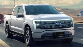 A gray 2022 Ford F-150 Lightning electric pickup truck is driving on the road.