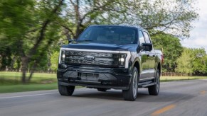 A black 2022 Ford F-150 Lightning Platinum is driving on the road.