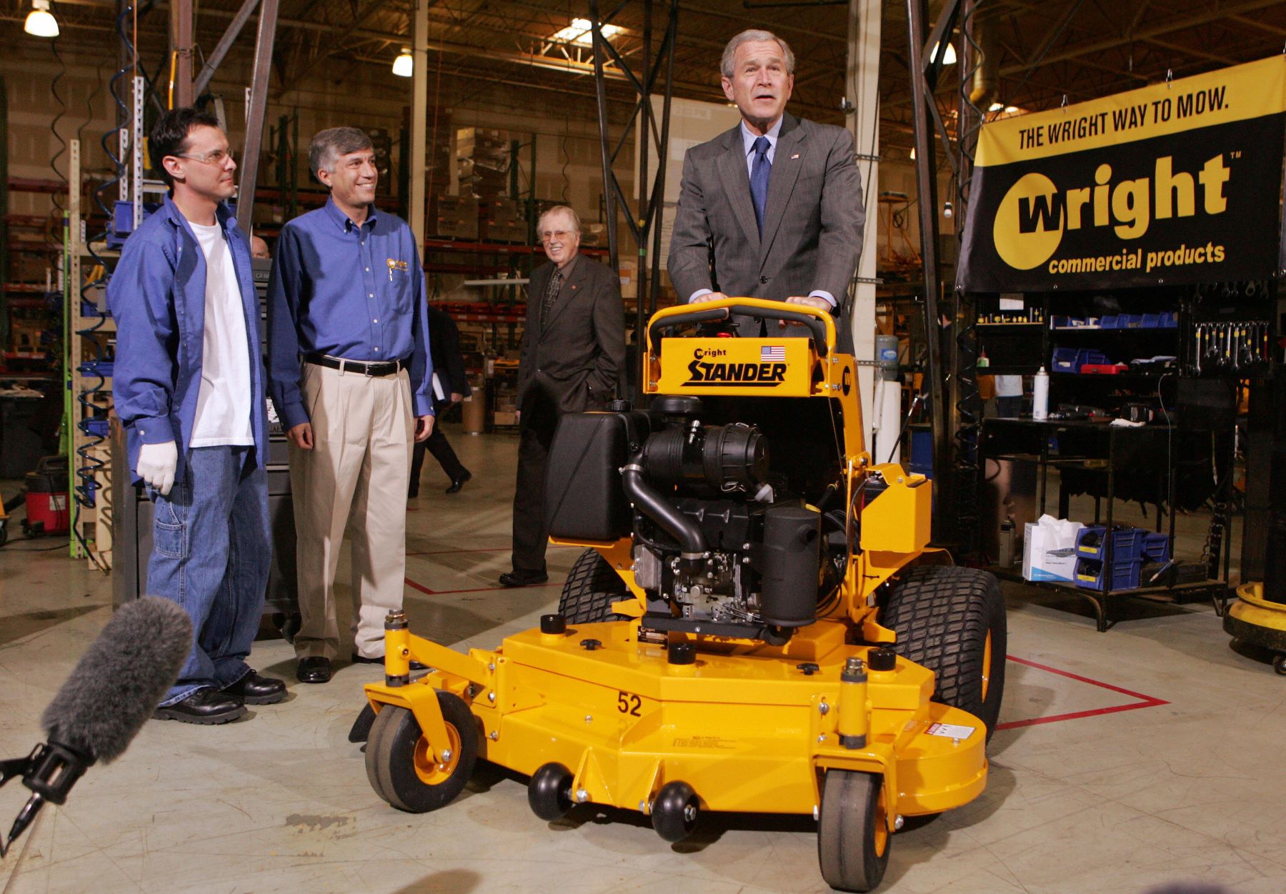 George W. Bush riding a stand-on lawn mower during a tour of Wright Manufacturing in Fredrick, Maryland