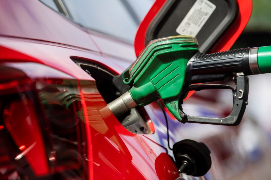 A person pumping gas, most likely experiencing high gas prices, into a red car.