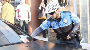 Parking enforcement officer leaving a ticket on a black car.