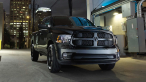 A black and gray Ram 1500 Classic full-size pickup truck parked near electrical maintenance equipment in a city at night