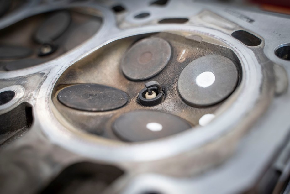 Closeup of a spark plug's electrodes protruding into a disassembled combustion chamber head, between the intake and exhaust valves.