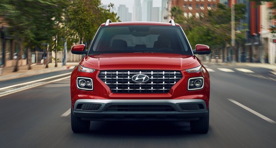 A red 2022 Hyundai Venue subcompact SUV is driving on the road. 