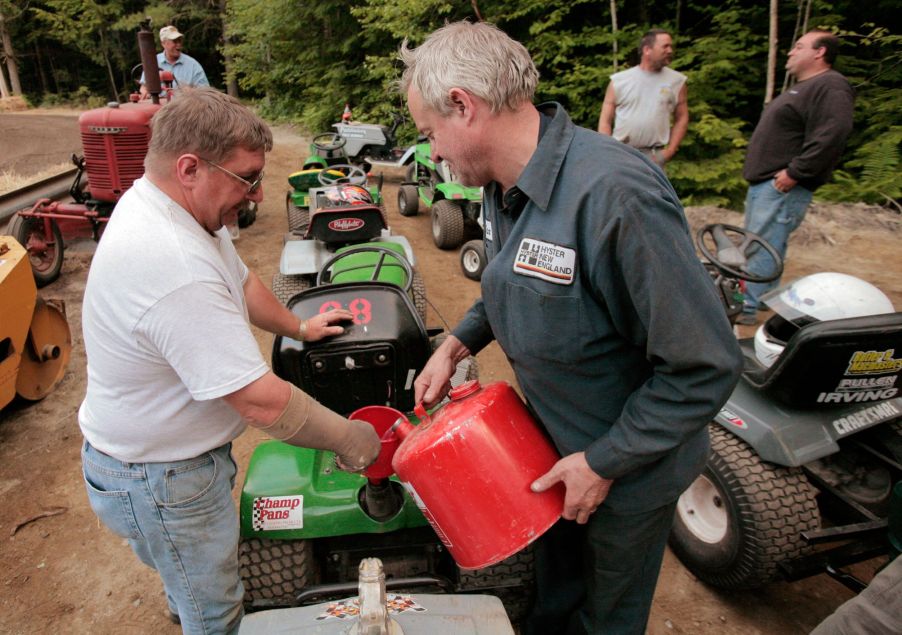 Mike Ramsey holding a funnel as Dan Bowley pours gasoline into a lawn mower at the Saco Pathfinder Snowmobile Club