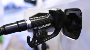 A white car being filled up by a black gas pump as gas prices continue going up.