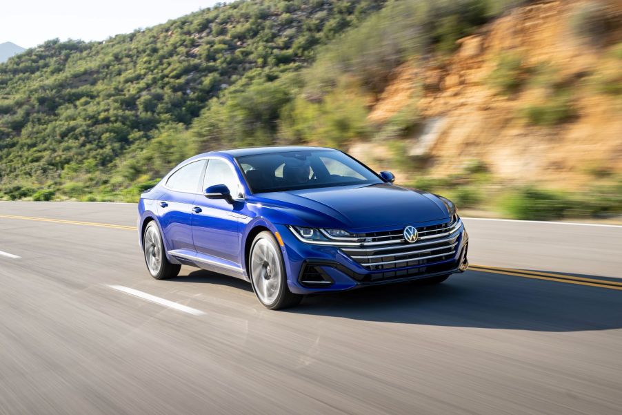 A blue 2022 Volkswagen Arteon executive car model driving on a highway near a cliffside of trees