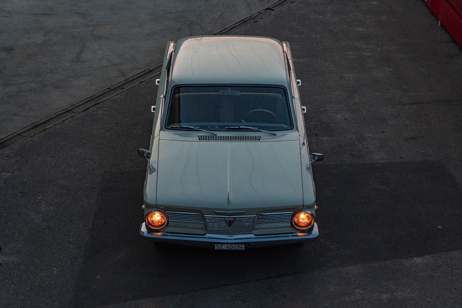 Plymouth valiant classic car parked on the pavement at twilight with its headlights on.