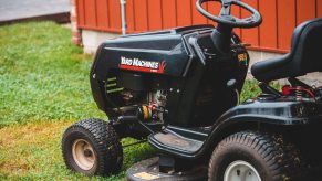 Black lawn tractor parked on a yard by a red shed wall.