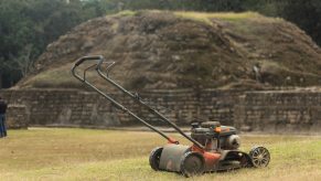 Walk-behind push lawn mower parked in front of a stone retaining wall on a freshly mowed lawn.