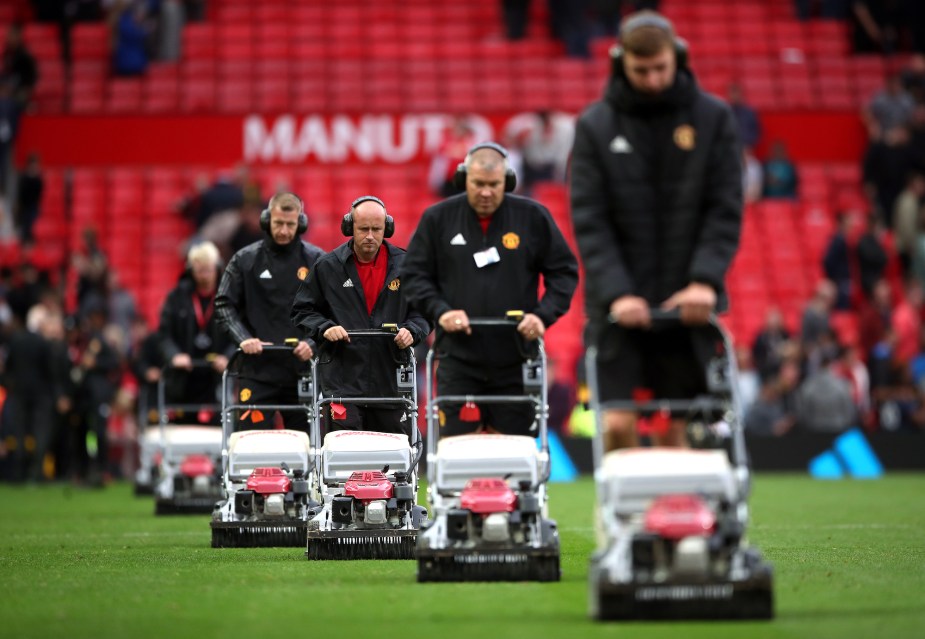 A row of people with gas powered lawn mowers. 