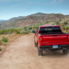 A red Chevy Silverado pickup truck driving on a sandy trail.