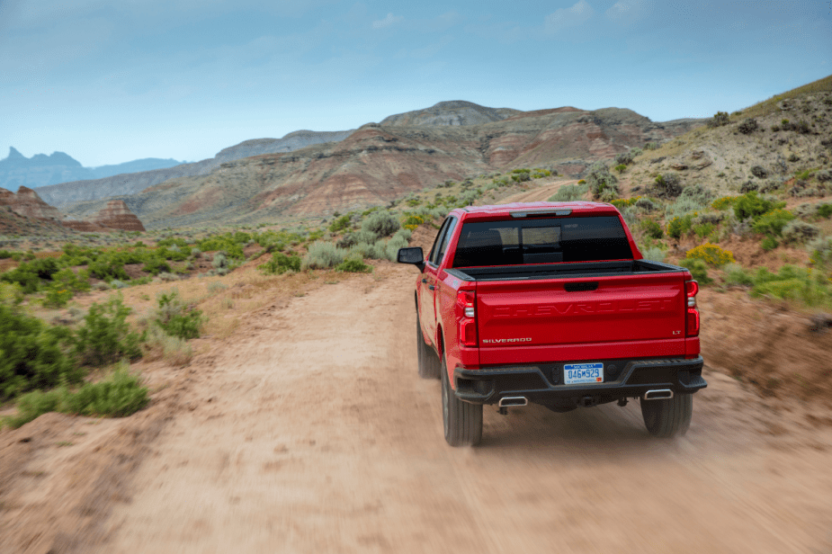 A red Chevy Silverado pickup truck driving on a sandy trail.