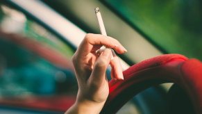 Closeup of a woman's hand holding a cigarette against the steering wheel of her car.