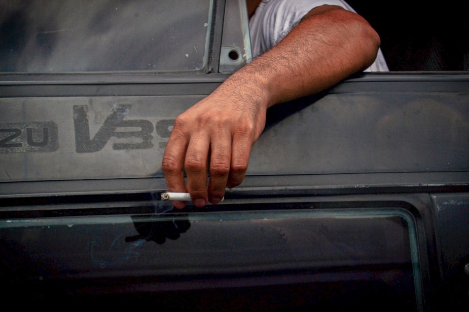 Closeup of a man's hand holding a cigarette while hanging out the window of his SUV.