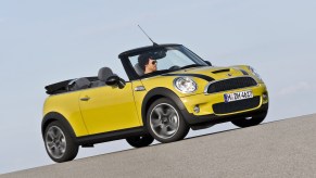 A yellow-with-black-stripes 2009 R57 Mini Cooper S Convertible with its roof down