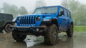 A blue mud-splattered 2021 Jeep Wrangler Unlimited Rubicon 4xe in a forest-side parking lot