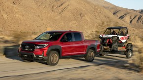 Red Honda Ridgeline pickup truck demonstrating its towing capacity by trailering in the desert, mountains visible in the background.